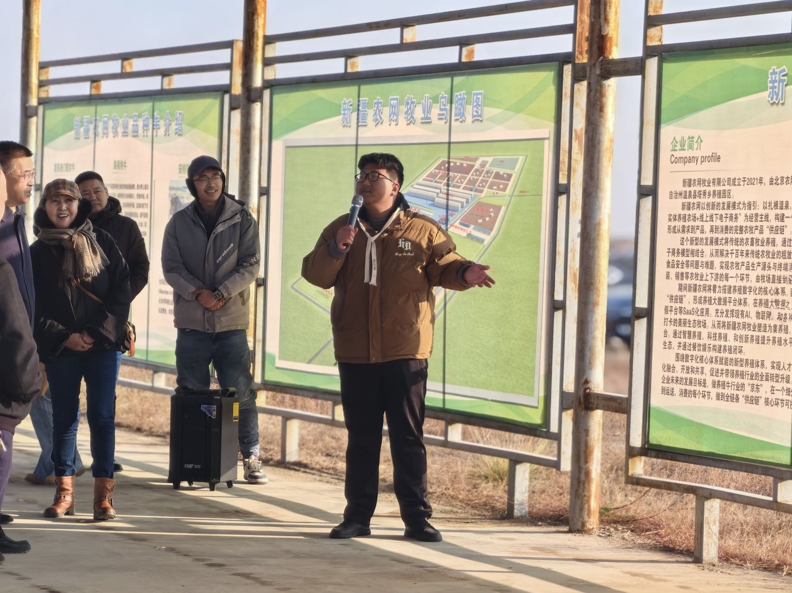 来访者在基地展板前听工作人员讲解，展板上是新疆农网牧业园区鸟瞰图与企业简介