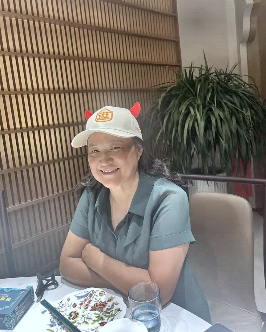 她戴着自家的米色帽子，坐在饭桌边，两只手搭在桌上。